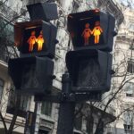 Pair of pedestrian crossing signals on a street pole, showing two adults holding hands in orange, with walk icons below.
