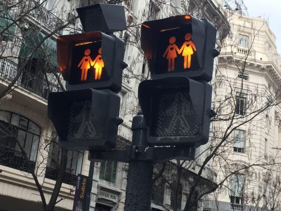 Pair of pedestrian crossing signals on a street pole, showing two adults holding hands in orange, with walk icons below.