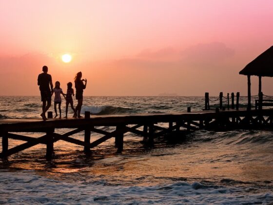 Silhouetted family walking on a wooden pier at sunset over the ocean edge.