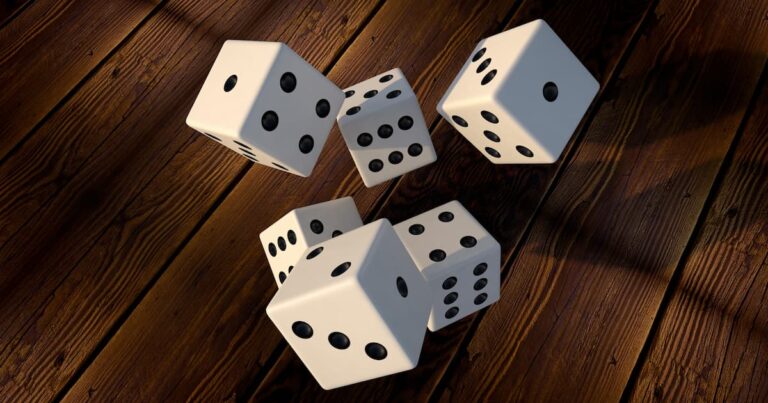 Five white dice with black pips tumble on a dark wooden surface, shadows visible underneath.