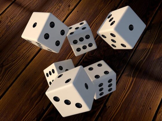 White dice with black pips tumbling through the air over a dark wooden game table, cast in warm light.